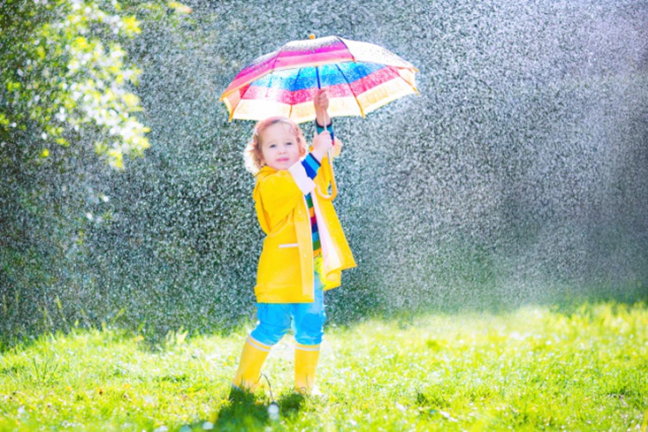 Funny toddler with umbrella playing in the rain